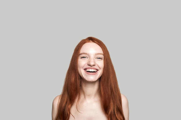 Retrato de belleza alegre de dama pelirroja bastante joven y positiva sonriendo a la cámara mientras