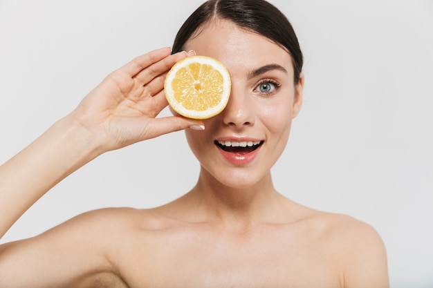 Retrato de belleza de una atractiva joven en topless aislada sobre pared blanca, mostrando rodajas de limón