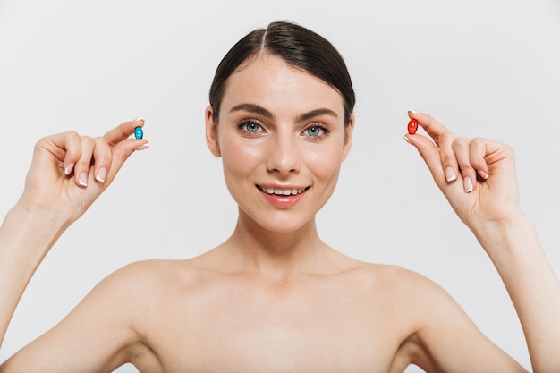 Retrato de belleza de una atractiva joven en topless aislada sobre una pared blanca, tomando pastillas de belleza