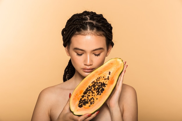 Retrato de belleza de una atractiva joven en topless que se encuentran aisladas sobre la pared beige, posando con papaya