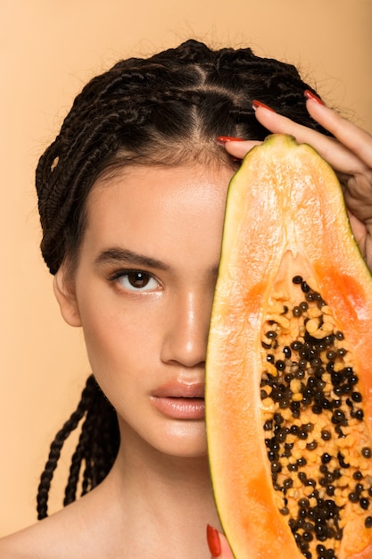 Retrato de belleza de una atractiva joven en topless que se encuentran aisladas sobre la pared beige, posando con papaya