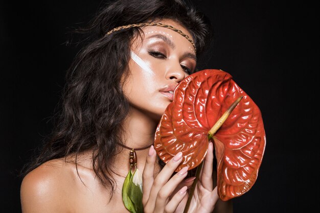 Retrato de belleza de una atractiva mujer morena joven sensual con accesorios tribales posando con flores tropicales aisladas