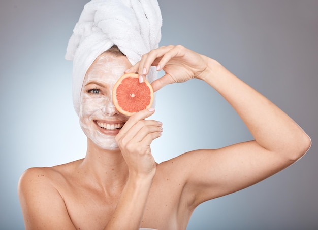 Retrato de belleza y facial con una mujer en el estudio sobre un fondo gris sosteniendo una rodaja de naranja para el cuidado natural Cuidado de la piel facial y cosméticos con una mujer posando para promover un producto de bienestar