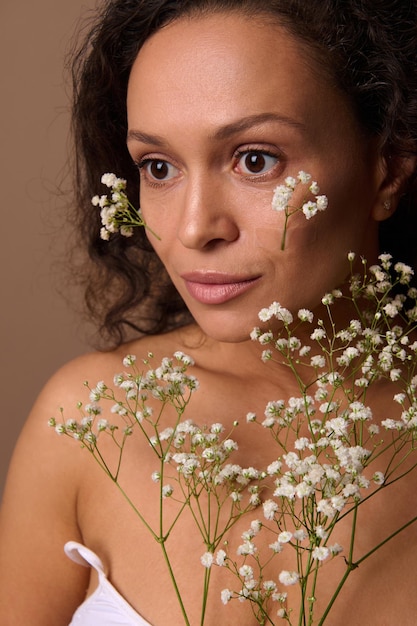 Retrato de belleza de una hermosa mujer hispana de cabello oscuro, serena y segura de sí misma, con una ramita de gypsophila blanca. Cuidado del cuerpo, positividad, sensualidad, confianza, autoaceptación, feminidad, concepto del día de la mujer