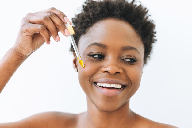 Retrato de belleza de una joven africana sonriente en ropa interior con aceite cosmético para la cara