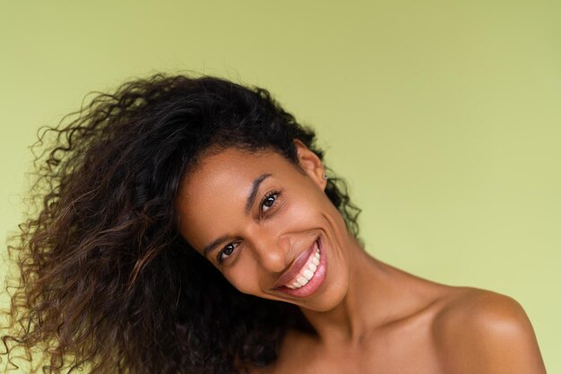 Retrato de belleza de una joven afroamericana en topless con hombros desnudos sobre fondo verde con piel perfecta y maquillaje natural