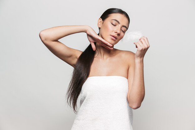 Retrato de belleza de una joven mujer morena atractiva sana que se encuentran aisladas, posando con una pluma