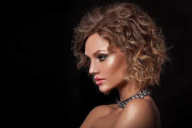 Retrato de belleza de una joven con la piel limpia de la cara. Cabello ondulado, fotografiado sobre un fondo negro.