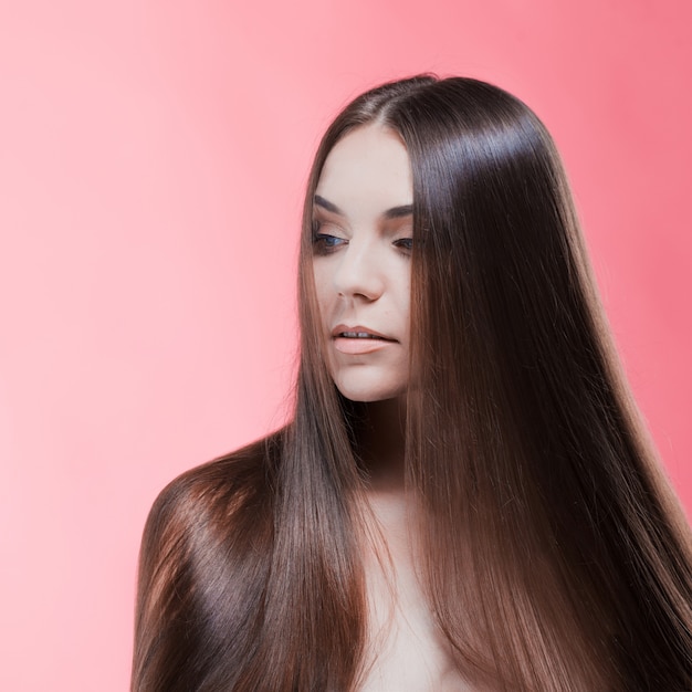 Retrato de belleza de morena con cabello perfecto, en una pared de color rosa. Cuidado del cabello