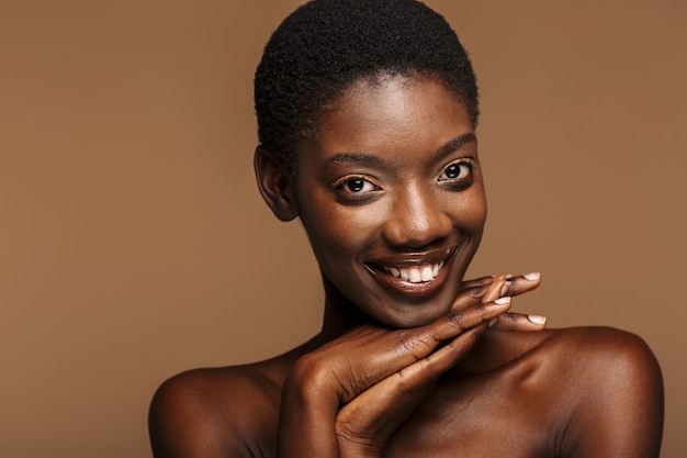 Retrato de belleza de mujer africana semidesnuda joven con pelo negro corto aislado en beige