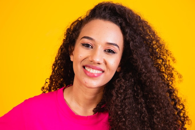 Retrato de belleza de mujer afroamericana con peinado afro y maquillaje glamour. Mujer brasileña. Raza mixta. Pelo RIZADO. Estilo de pelo. Fondo amarillo