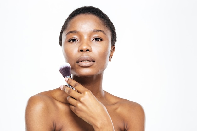 Retrato de belleza de mujer afroamericana sosteniendo pincel de maquillaje aislado sobre un fondo blanco.