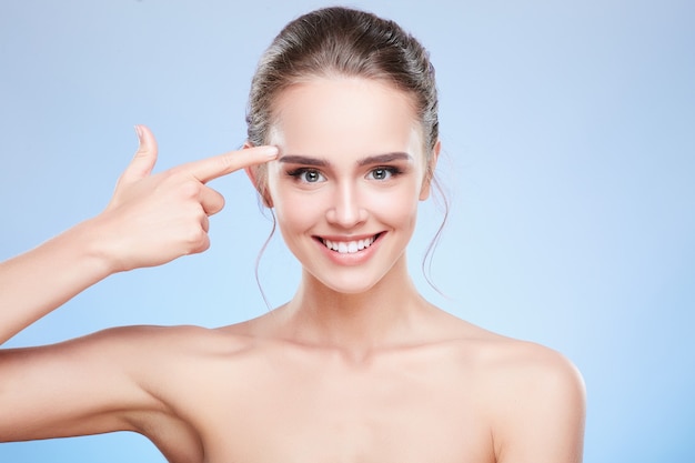 Retrato de belleza de mujer apuntando al templo y sonriendo. Cabeza y hombros de mujer con maquillaje nude, concepto de belleza.