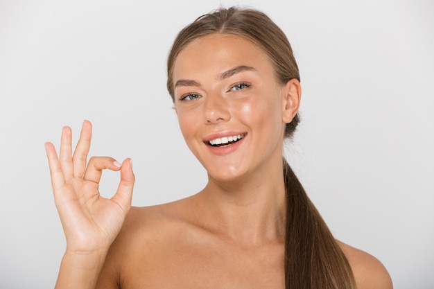 Retrato de belleza de mujer bonita sin camisa con cabello largo castaño sonriendo y mostrando el signo de ok, aislado