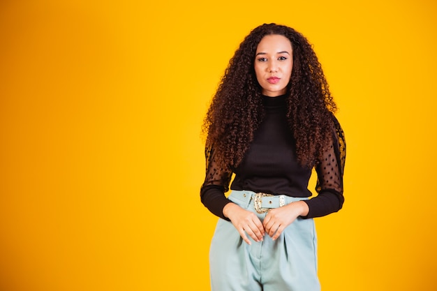 Retrato de belleza de una mujer brasileña con peinado afro y maquillaje glamour. Mujer latina. Raza mixta. Pelo RIZADO. Estilo de pelo. Fondo amarillo