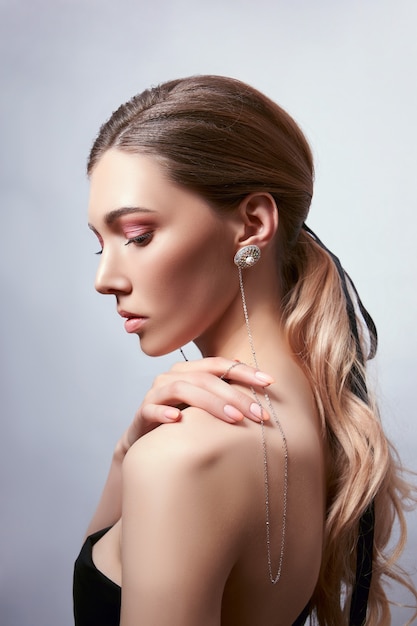 Retrato de belleza de una mujer con cabello largo, aretes en las orejas y joyas caras en sus manos