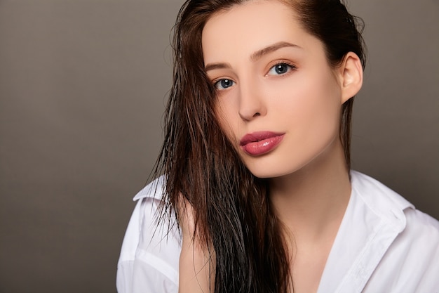 Retrato de belleza de mujer con una camisa blanca y cabello mojado sobre fondo marrón