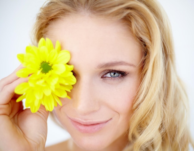 Retrato de belleza y mujer con una flor en un estudio con una rutina cosmética natural y facial Sonrisa feliz y modelo femenino joven con una planta floral amarilla para facial aislada por fondo blanco