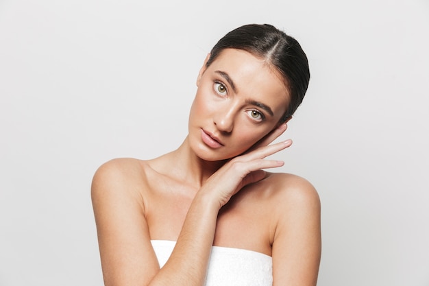 Retrato de belleza de una mujer joven y bonita envuelta en una toalla que se encuentran aisladas, posando