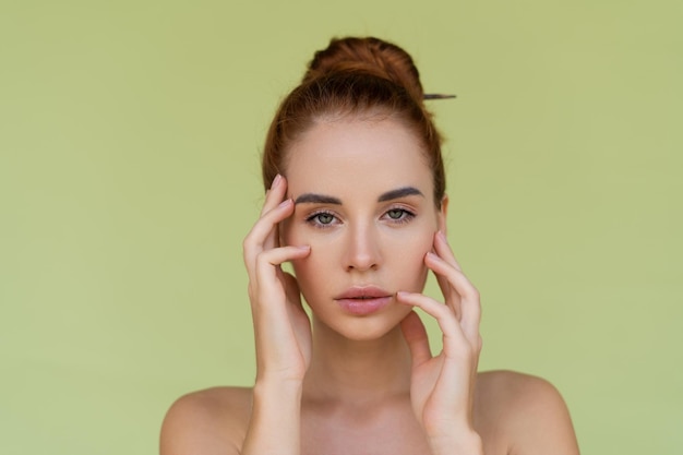 Retrato de belleza de mujer joven de pelo rojo en topless con hombros desnudos sobre fondo verde con piel perfecta y maquillaje natural