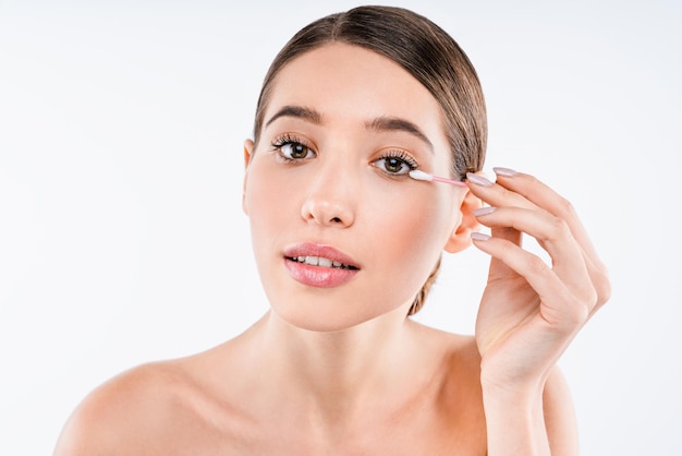 Retrato de belleza de mujer joven quitando maquillaje con hisopo de algodón aislado sobre fondo blanco.