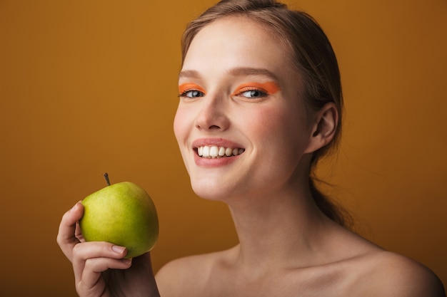 Retrato de belleza de una mujer joven rubia con maquillaje que se encuentran aisladas, comiendo manzana verde