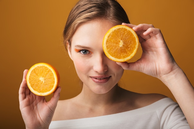 Retrato de belleza de una mujer joven rubia con maquillaje que se encuentran aisladas, mostrando dos mitades de una fruta naranja