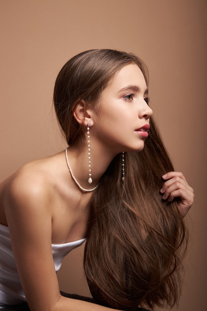 Retrato de belleza de una mujer con joyas, aretes en las orejas y collar alrededor del cuello. Piel facial perfecta y limpia, cosmética natural.