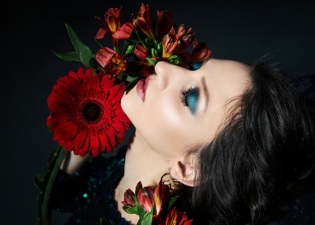 Retrato de belleza de una mujer con maquillaje de noche hermosa y flores en la cara