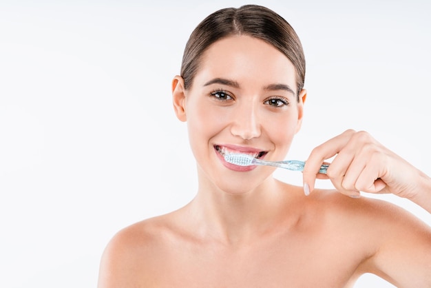 Retrato de belleza de una mujer medio desnuda feliz cepillándose los dientes con cepillo de dientes y mirando a la cámara