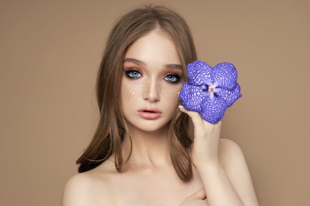 Retrato de belleza de una mujer con una orquídea Vanda azul en la mano. Cosmética natural hecha de pétalos de flores, limpia la delicada piel de la cara de la niña.