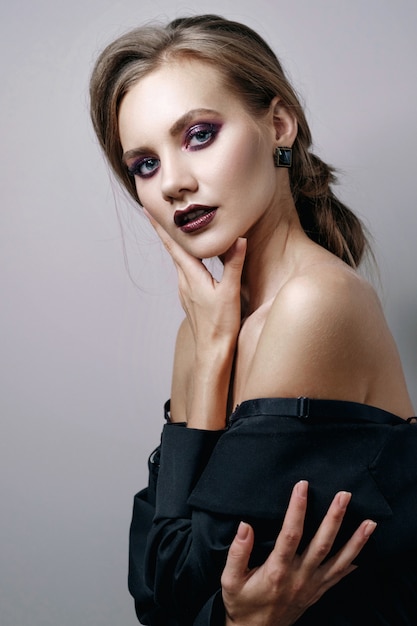 Retrato de belleza de mujer en pared gris, modelo de moda con piel limpia y hermosos labios, maquillaje de ojos ahumados de color morado oscuro