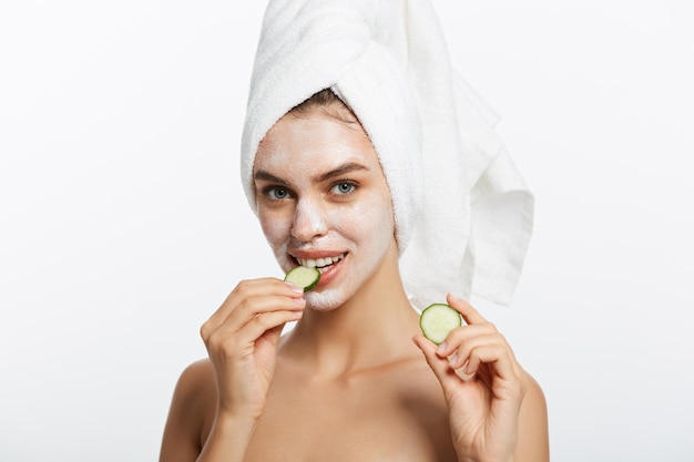 Retrato de belleza de mujer sonriente con toalla en la cabeza y rodaja de pepino en la mano aislado en blanco