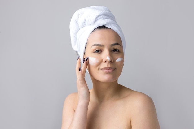 Retrato de belleza de mujer con toalla blanca en la cabeza aplica crema en la cara Cuidado de la piel limpieza eco cosmética orgánica spa relax concepto