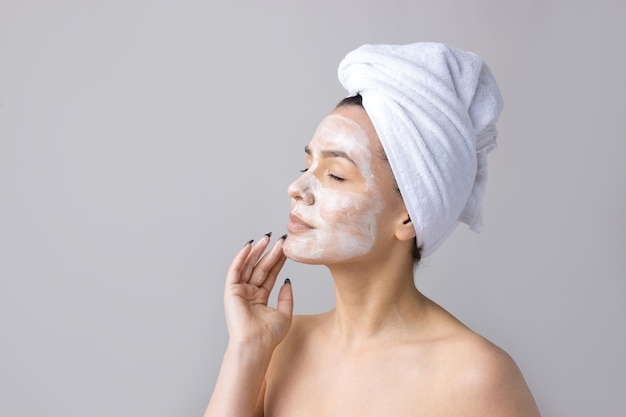 Foto retrato de belleza de mujer con toalla blanca en la cabeza aplica crema en la cara limpieza de cuidado de la piel