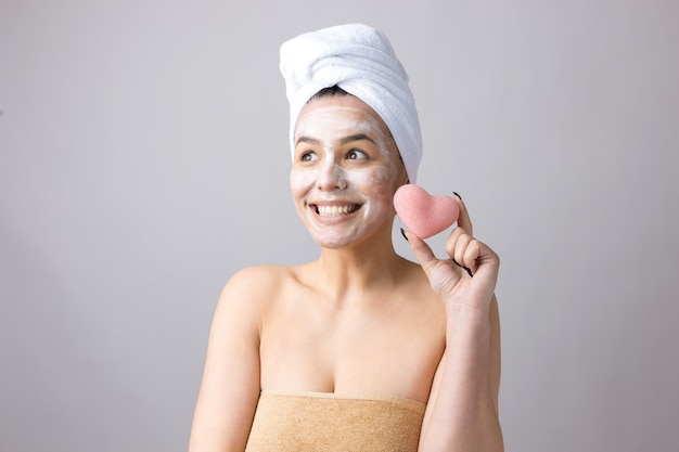 Retrato de belleza de mujer con toalla blanca en la cabeza con una esponja para un cuerpo a la vista de un corazón rosa