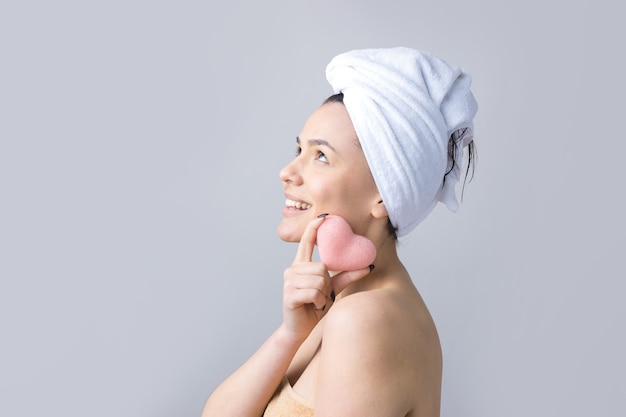 Retrato de belleza de mujer con toalla blanca en la cabeza con una esponja para un cuerpo a la vista de un corazón rosa