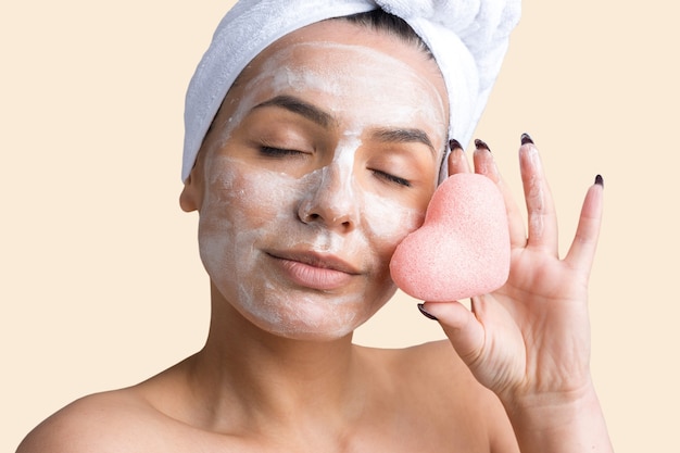 Retrato de belleza de mujer con toalla blanca en la cabeza con una esponja para un cuerpo a la vista de un corazón rosa