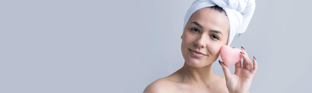 Retrato de belleza de mujer en toalla blanca en la cabeza con una esponja para un cuerpo a la vista de un corazón rosa