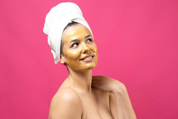 Retrato de belleza de mujer en toalla blanca en la cabeza con máscara nutritiva dorada en la cara Cuidado de la piel limpieza eco cosmética orgánica spa relax concepto