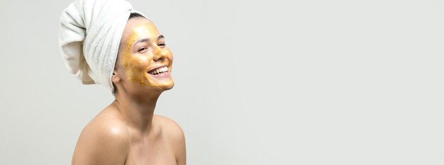 Retrato de belleza de mujer en toalla blanca en la cabeza con máscara nutritiva dorada en la cara Cuidado de la piel limpieza eco cosmética orgánica spa relax concepto