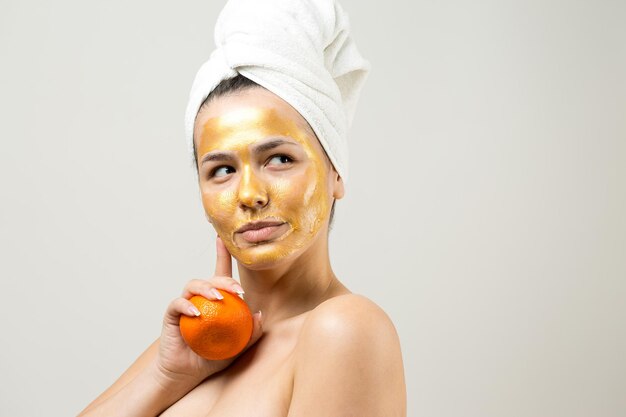 Retrato de belleza de mujer con toalla blanca en la cabeza con máscara nutritiva dorada en la cara