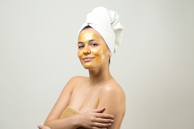 Retrato de belleza de mujer en toalla blanca en la cabeza con máscara nutritiva dorada en la cara