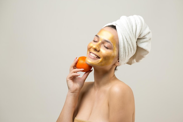 Retrato de belleza de mujer en toalla blanca en la cabeza con máscara nutritiva dorada en la cara