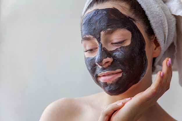 Retrato de belleza de mujer en toalla en la cabeza aplicando mascarilla nutritiva negra en la cara, fondo blanco aislado. Cuidado de la piel limpieza eco cosmética orgánica spa relax concepto