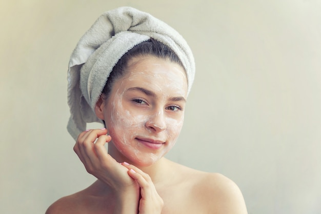 Retrato de belleza de mujer en toalla en la cabeza con máscara nutritiva blanca o crema en la cara, fondo blanco aislado