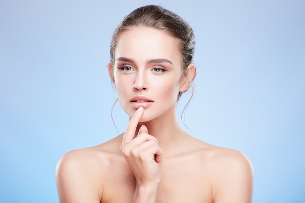 Retrato de belleza de mujer tocando el labio inferior y mirando con recelo. Cabeza y hombros de mujer con maquillaje nude, concepto de belleza.