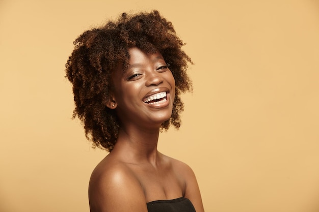 Retrato de belleza de una niña de etnia africana que se ríe con una piel limpia y saludable en un beige aislado