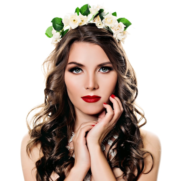 Retrato de belleza de niña con pelo largo y rizado y corona de flores en la cabeza sobre fondo blanco.