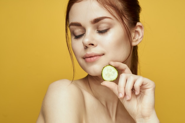 Retrato de belleza de niña con pepinos para hidratar la piel del rostro en las manos